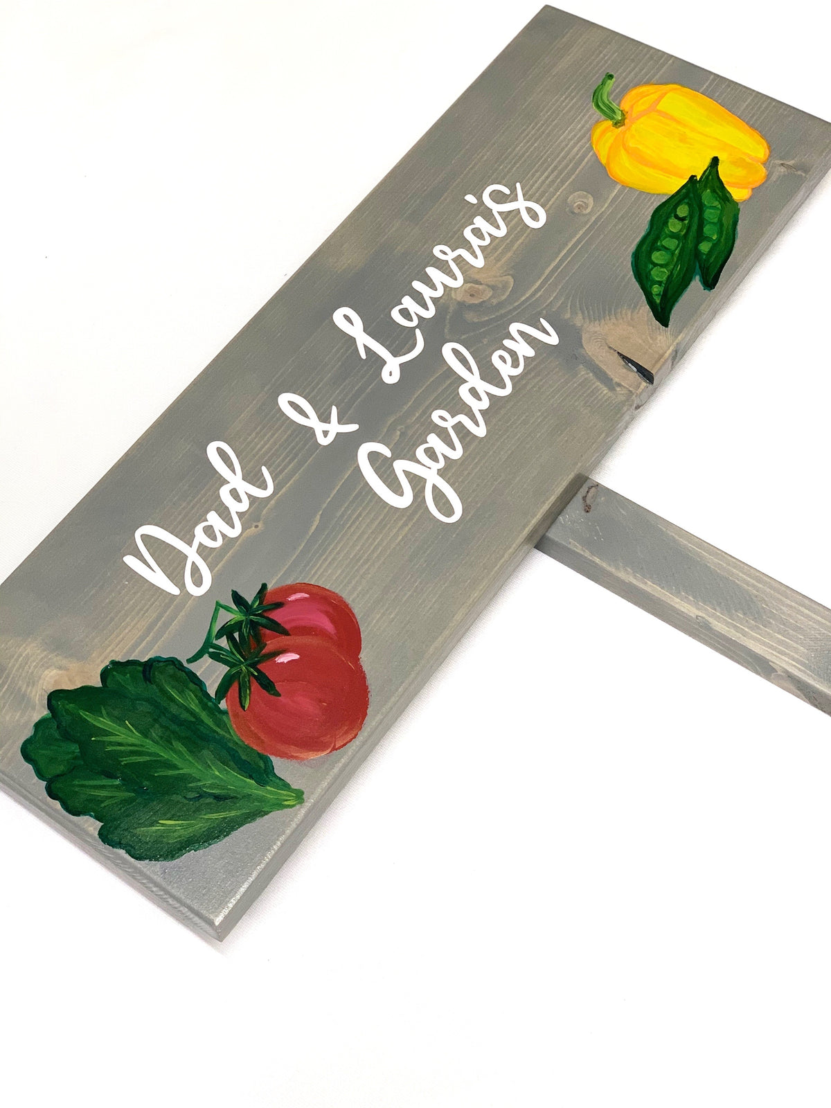 Large custom wooden garden sign painted gray with white cursive letters and colorful vegetable illustrations on wood grain background