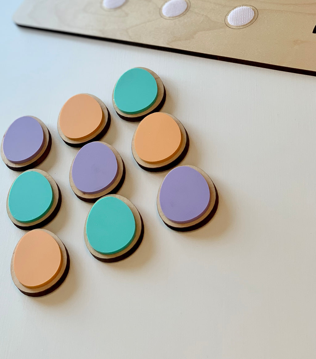 Wooden cookie-shaped pieces in pastel purple, teal, and peach with velcro backing next to wooden cookie sheet edge