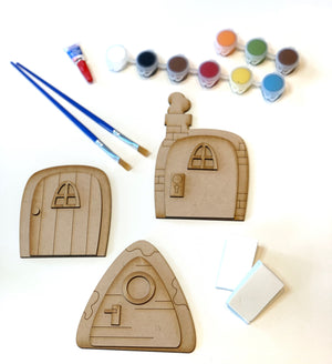 Unpainted wooden fairy doors DIY kit with two paintbrushes, eight small paint pots, and two white sponges on white background