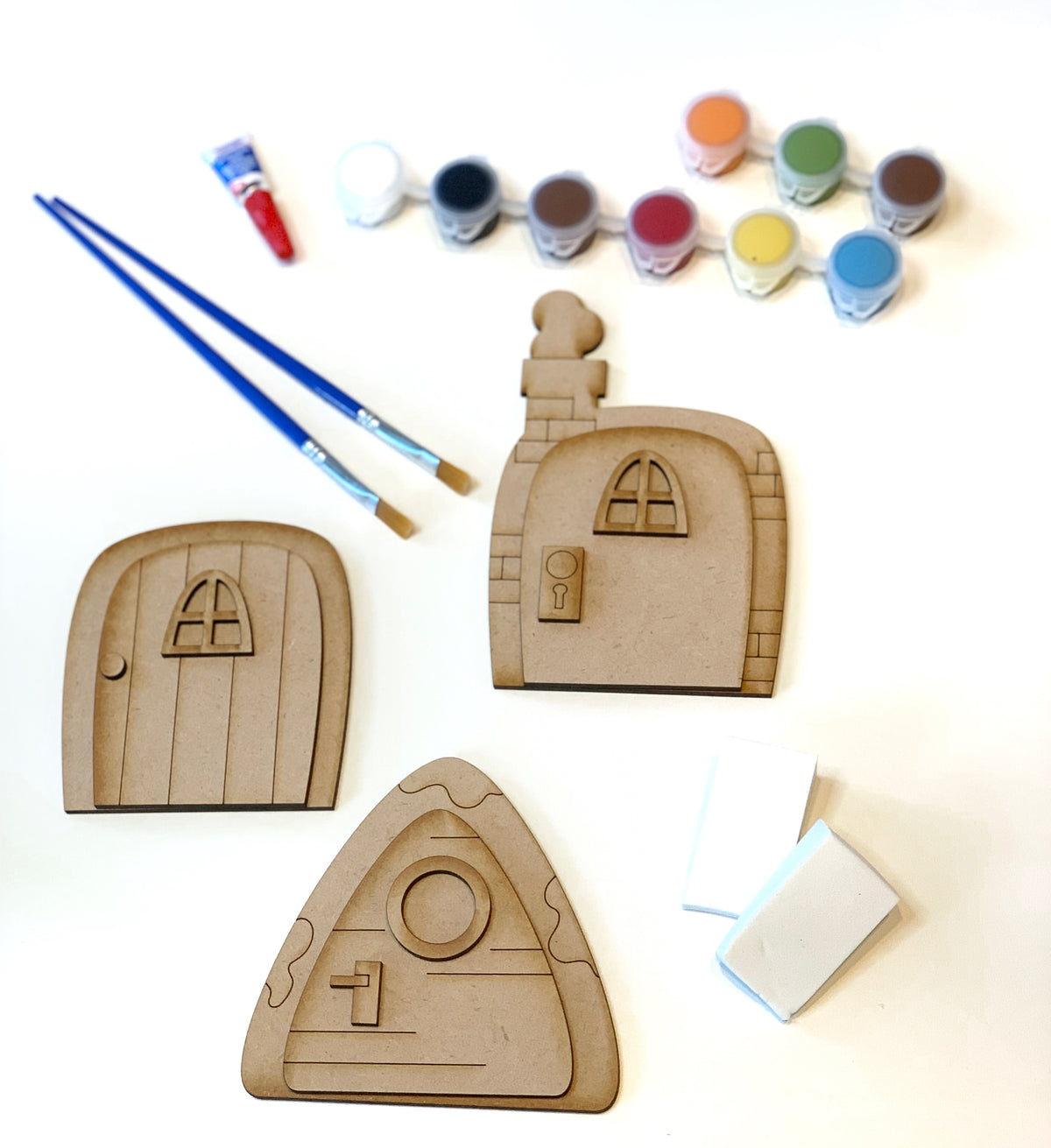 Unpainted wooden fairy doors DIY kit with two paintbrushes, eight small paint pots, and two white sponges on white background