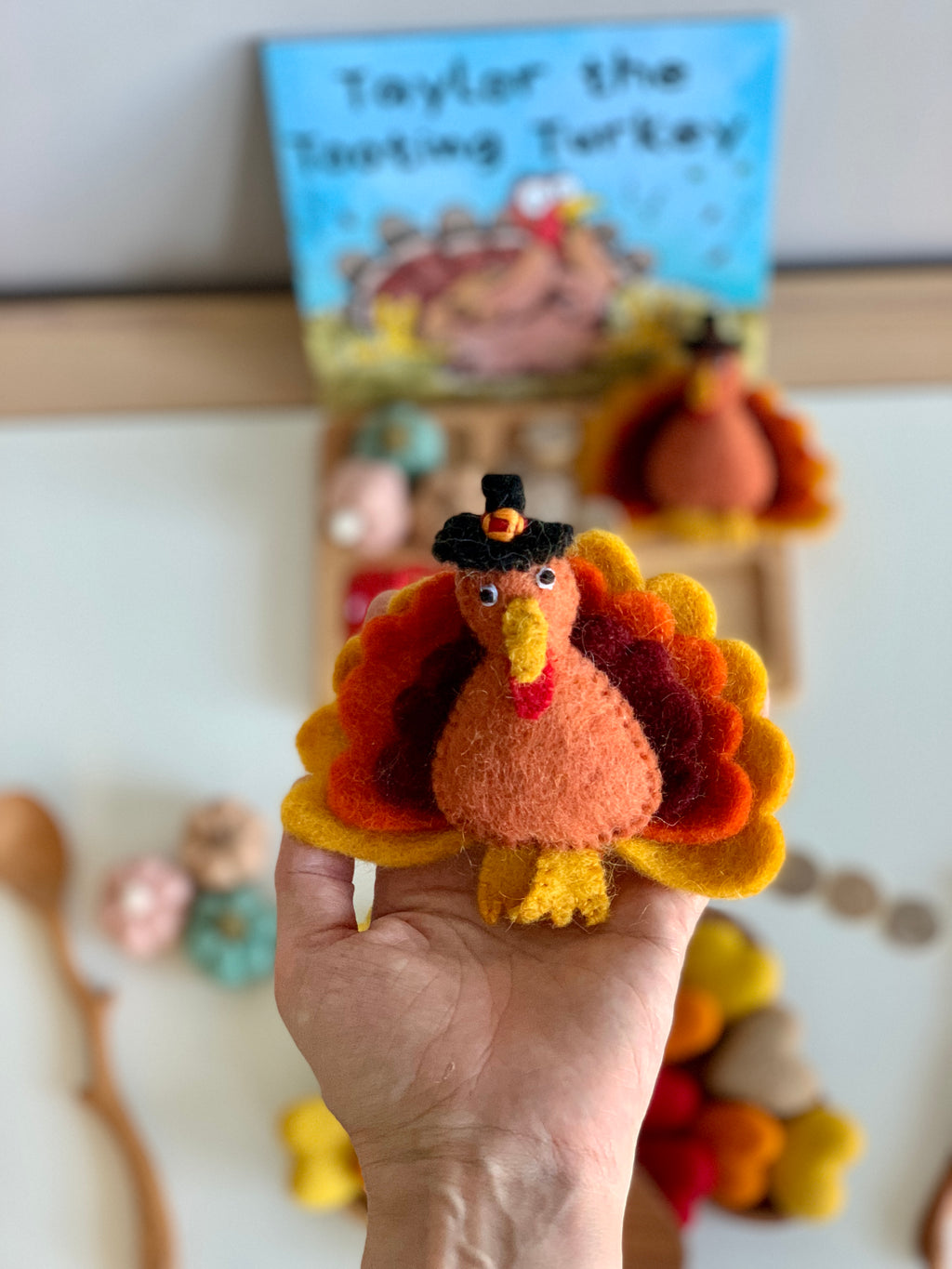 Handmade felt turkey with orange, red, yellow feathers and black pilgrim hat held in hand on blurred background