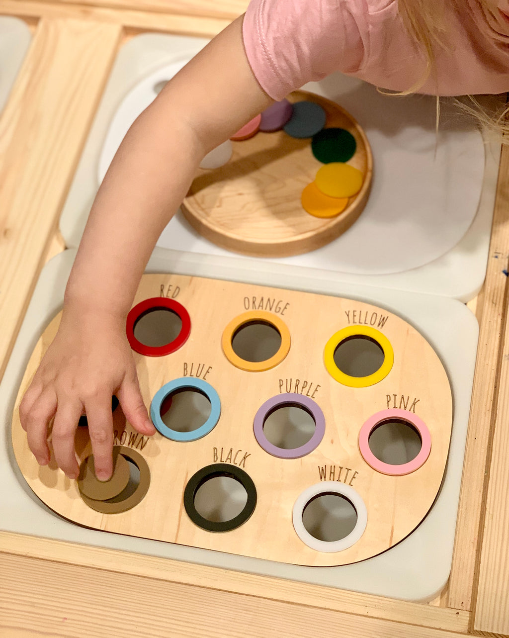 Child’s hand placing felt ball in natural wooden colour sorting Flisat table bin lid with colour names and circles