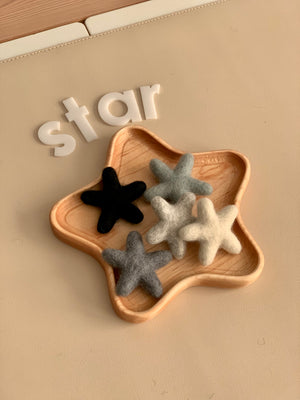 Neutral felt stars in shades of gray, black, and cream arranged in a wooden star-shaped dish on beige surface