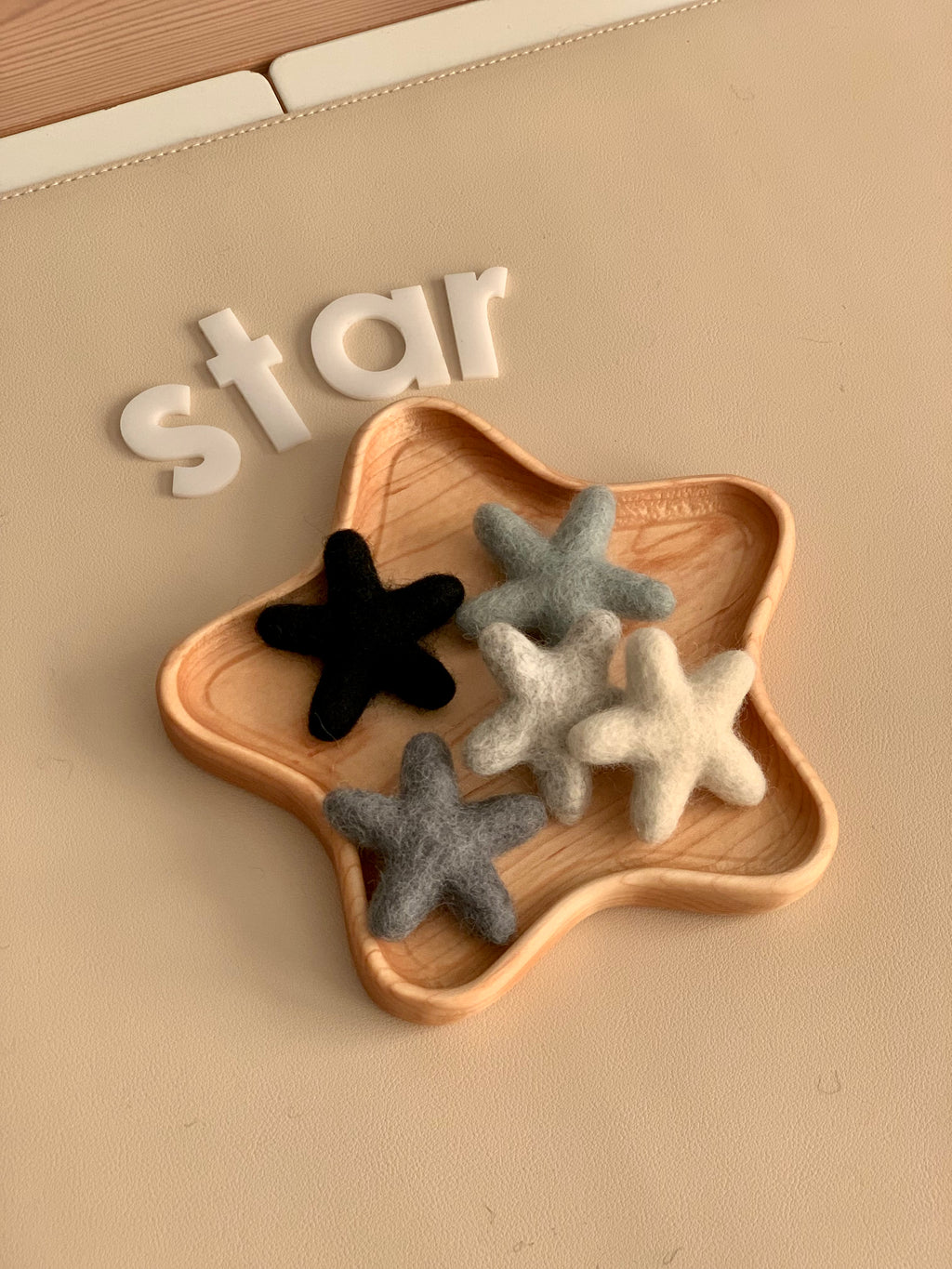 Neutral felt stars in shades of gray, black, and cream arranged in a wooden star-shaped dish on beige surface