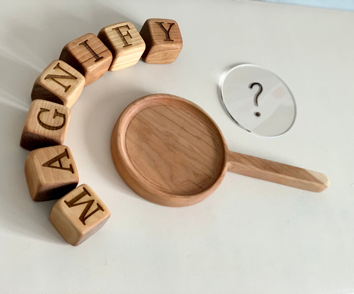 Wooden frying pan sensory tray with clear magnifying glass and wooden letter cubes spelling magnify on white surface