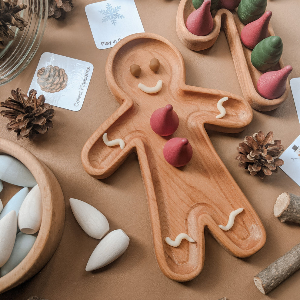 Natural wooden person-shaped sensory tray with smiling face and clay cones and swirls on a beige surface with pinecones and cards