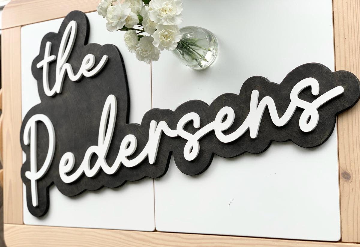 Custom wooden wedding backdrop sign with white cursive last name letters on black layered wood background