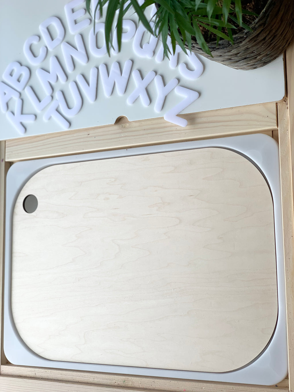 Maple plywood Wood Flisat table bin lid insert with rounded edges on wood frame with white plastic letters and green plant nearby