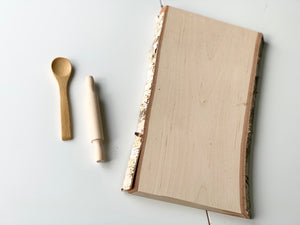 Live edge wooden tray with clear coat finish next to small wooden spoon and rolling pin on white background