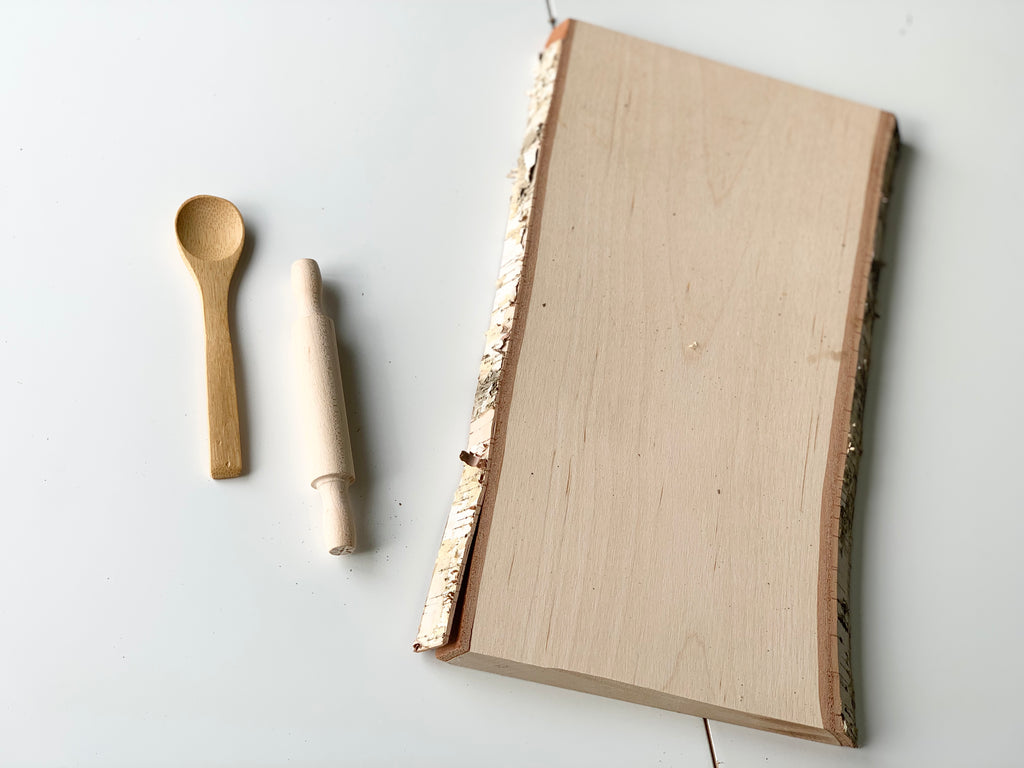 Live edge wooden tray with clear coat finish next to small wooden spoon and rolling pin on white background