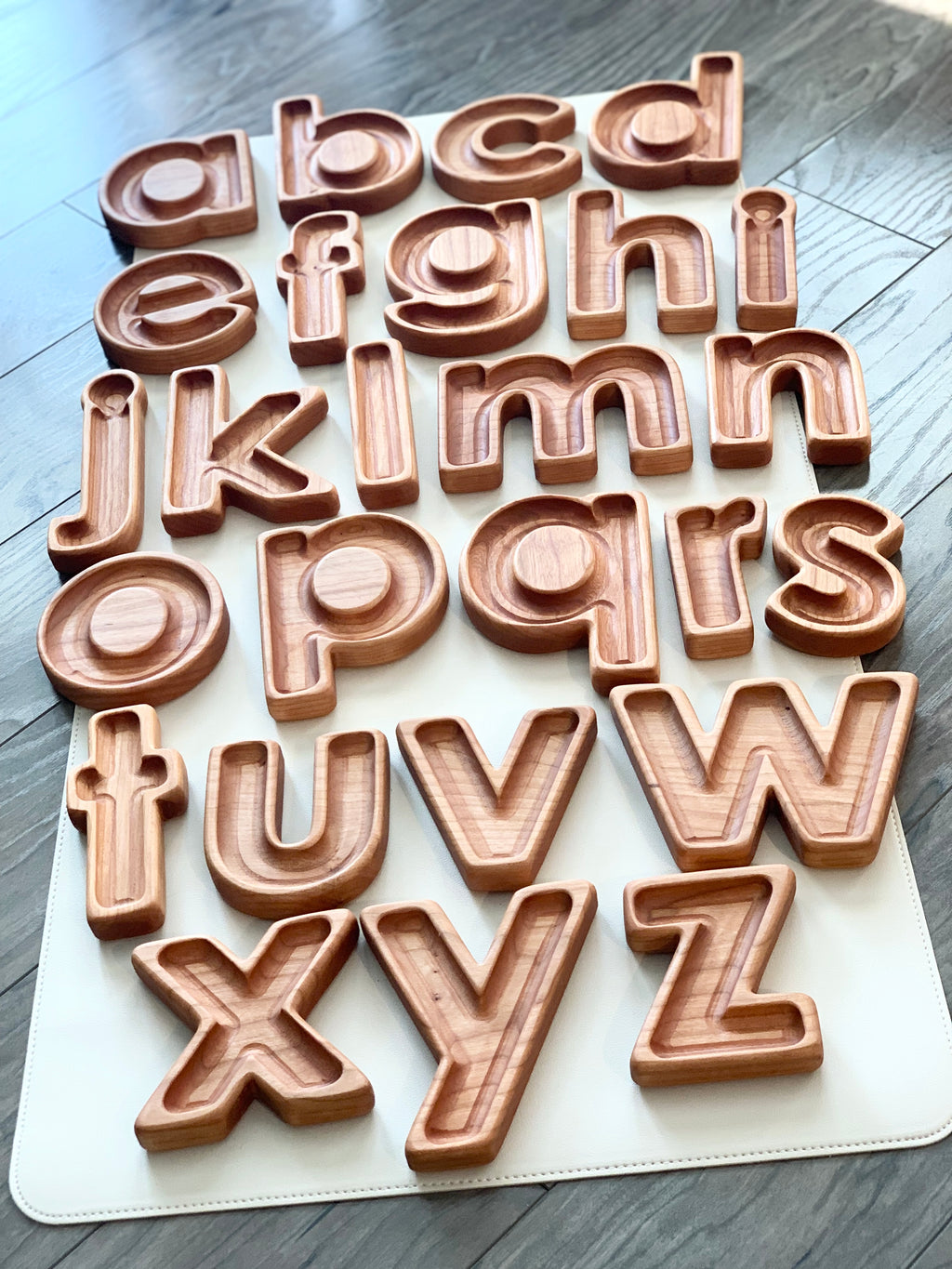 Set of natural wooden lowercase alphabet letter sensory trays arranged on white mat on wood floor