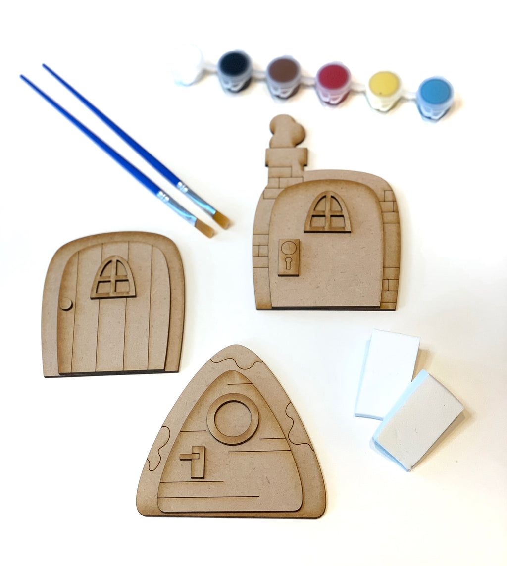 DIY fairy door kit with three unfinished wooden doors, two paintbrushes, six paint pots, and erasers on white background