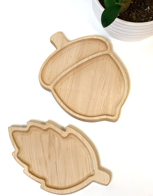 Two natural wooden sensory trays shaped like an acorn and a leaf on white background with plant pot edge visible
