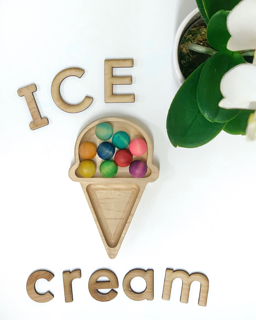 Small wooden ice cream cone shaped sensory tray filled with colorful wooden balls and wooden letters on white surface
