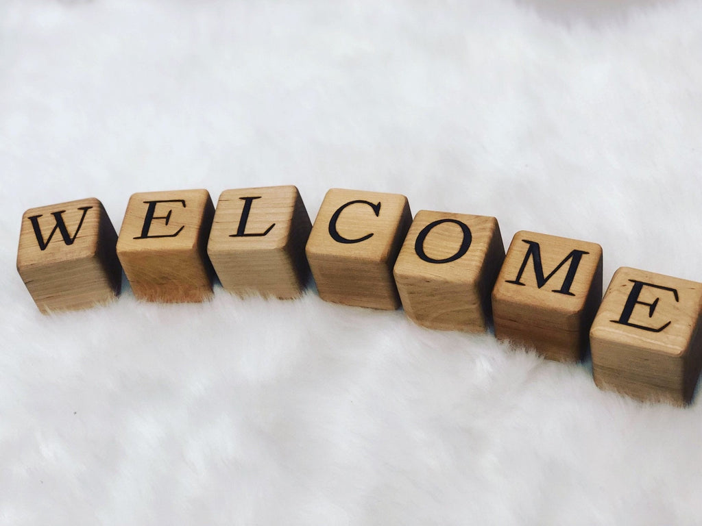 Natural wooden 1.5-inch blocks with engraved black letters spelling WELCOME arranged on white fabric background