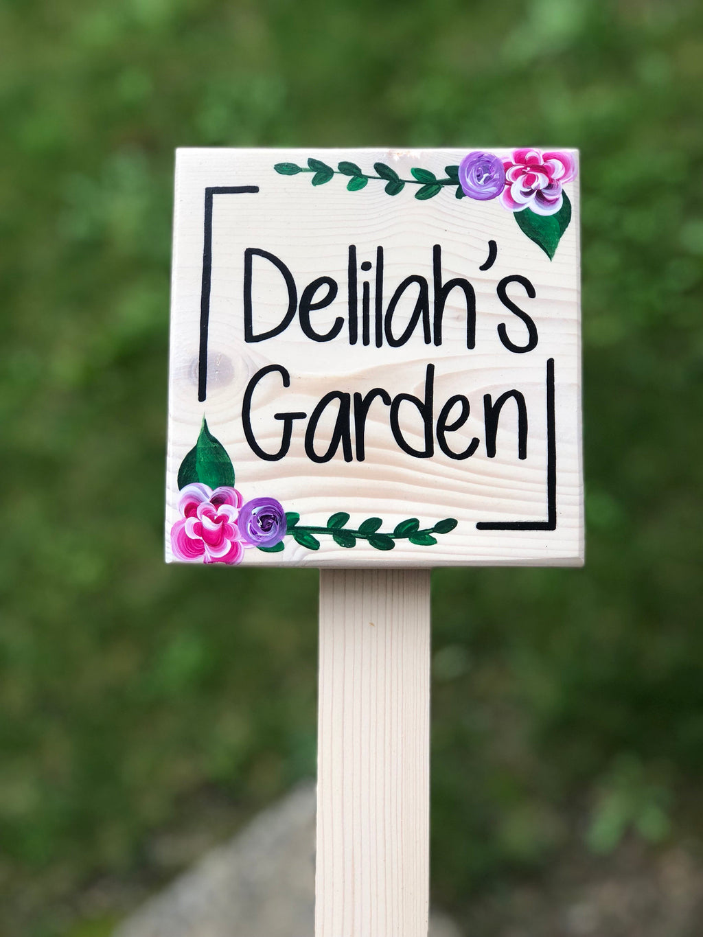 Small square wooden garden sign with black lettering and hand-painted pink and purple floral accents on natural wood background