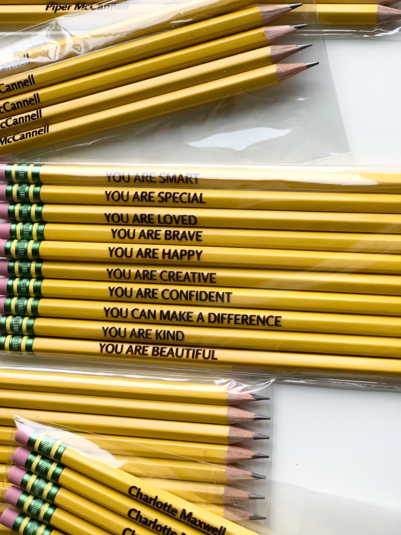 Set of 10 yellow affirmation pencils with inspirational black text and pink erasers arranged on white background