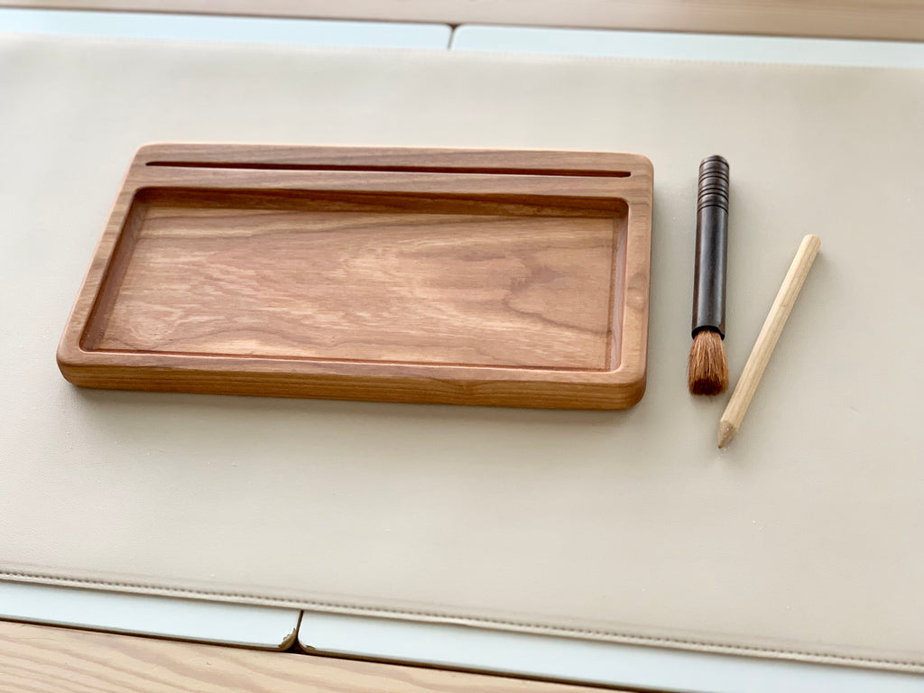 Rectangular wooden sensory tray with natural wood grain, and two wooden stylus tools on beige surface