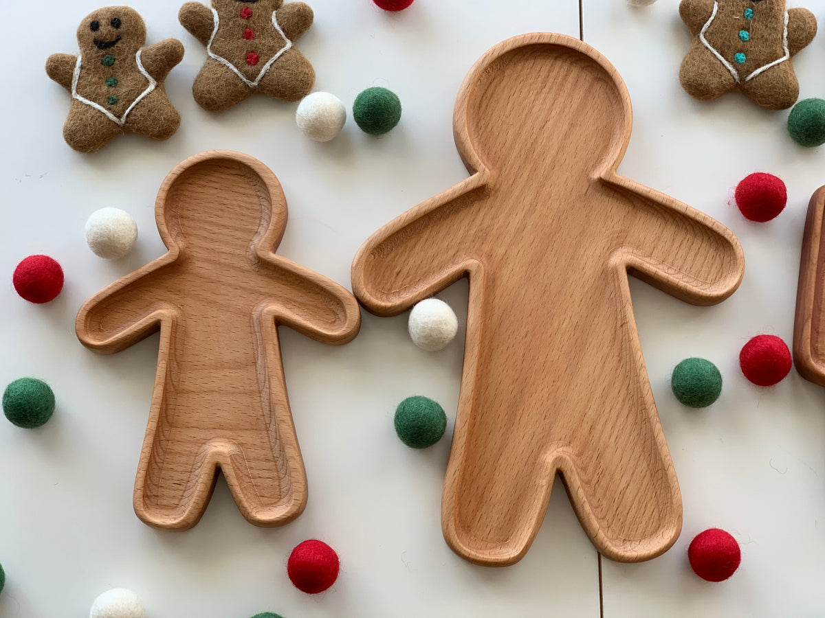 Natural wooden person-shaped plates of two sizes surrounded by felt balls and gingerbread decorations on white surface