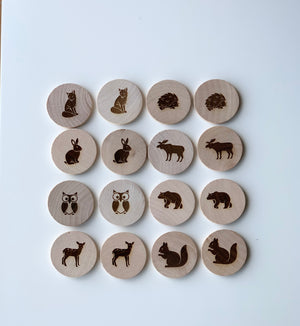 Natural wooden memory game discs with engraved woodland animal illustrations arranged in rows on white background