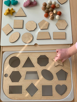 Child’s hand placing wooden star shape into Flisat table top shape sorter insert with various wooden shapes on white surface