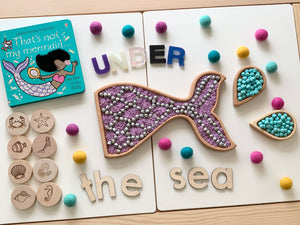 Mermaid tail sensory tray and wooden letters spelling UNDER the sea with colorful felt balls and ocean stamp blocks on white background
