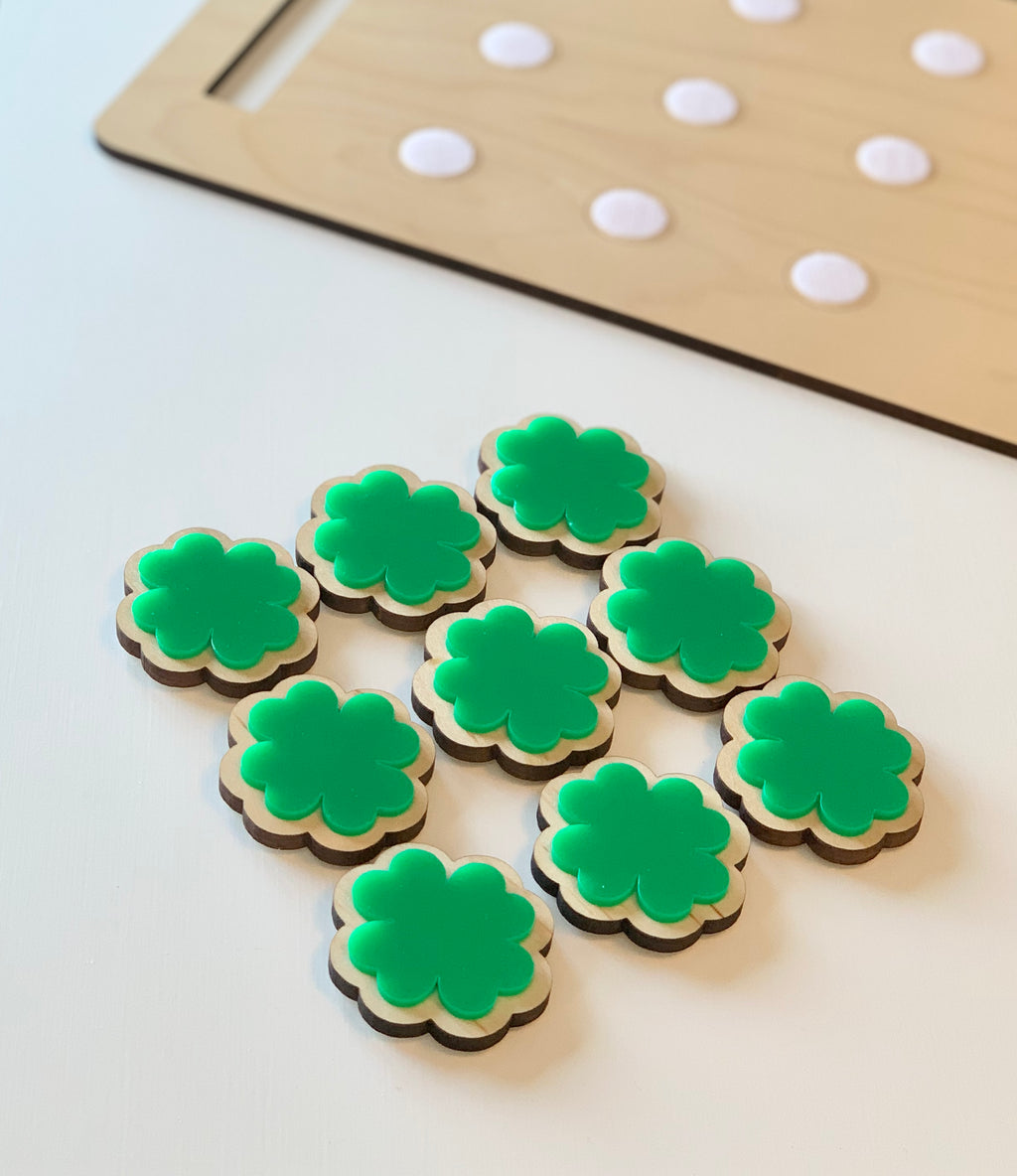 Wooden cookie sheet with ten green four-leaf clover-shaped cookie pieces featuring velcro backing on white surface
