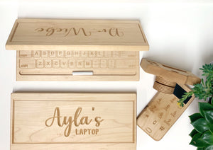 Natural wooden toy laptop with engraved keyboard and personalized lid alongside a rotating lens wooden toy camera on white surface