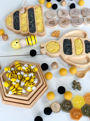 Natural wooden nesting hexagon plates with yellow and black rice and toy bees on white background
