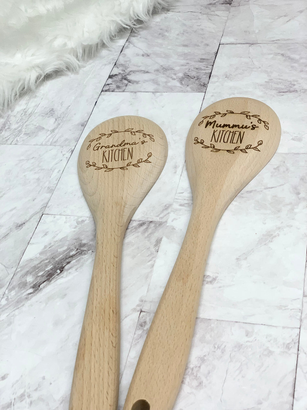 Two personalized wooden spoons engraved with "Grandma's Kitchen" and "Mummu's Kitchen" on light wood surface