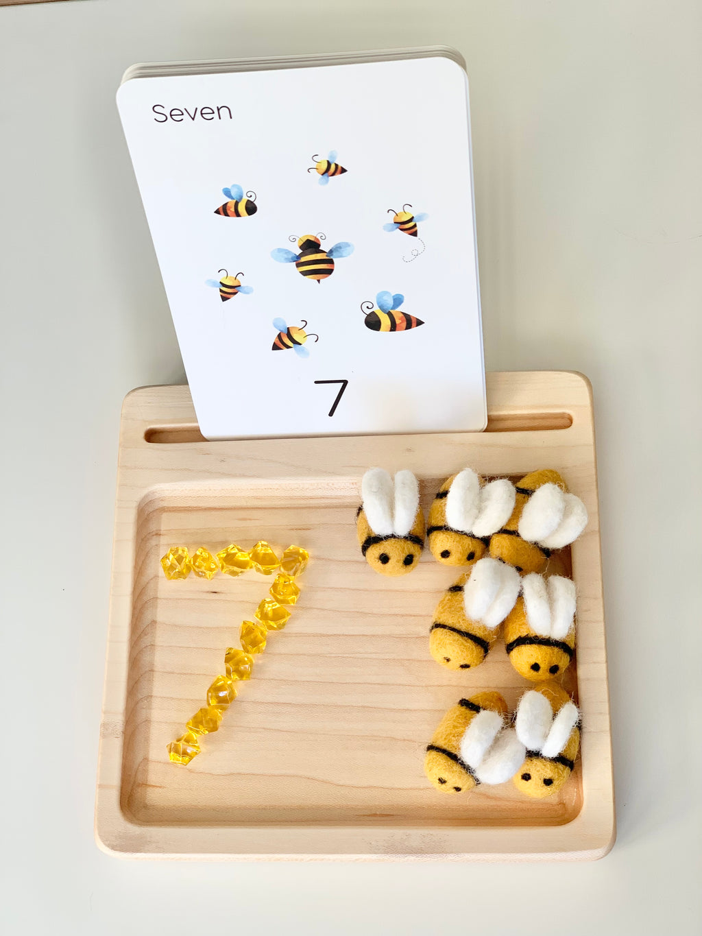 Wooden sensory tray with seven felt bees and yellow gems arranged to form number seven with flash card in back slot