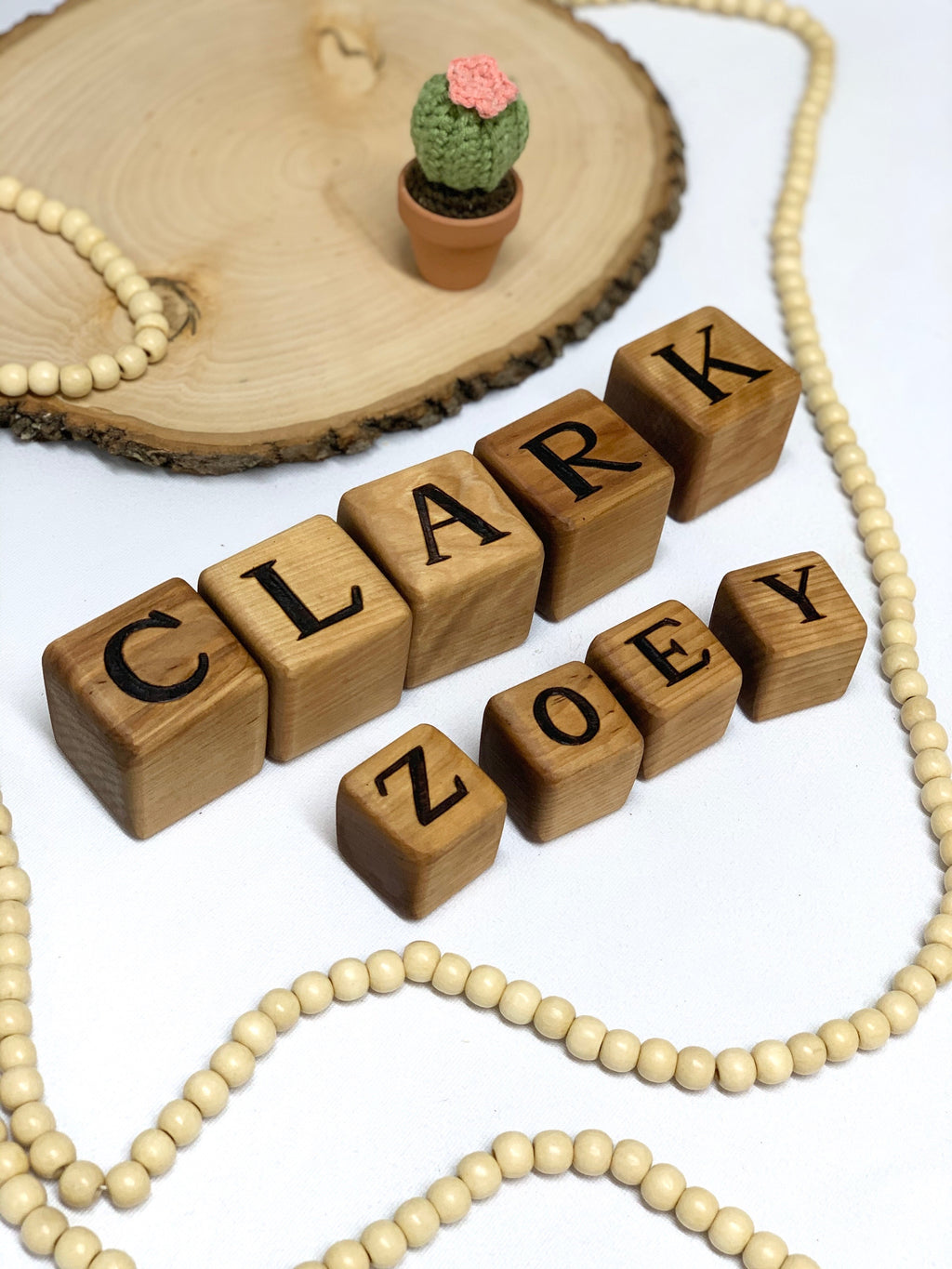Custom wooden 1.5-inch alphabet blocks with engraved black letters arranged on white surface with decorative beads and wooden slice background