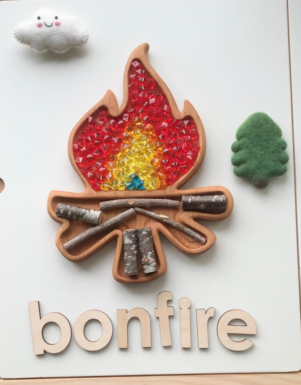 Wooden campfire shaped sensory tray with red and yellow gem flames and natural wood sticks on white background