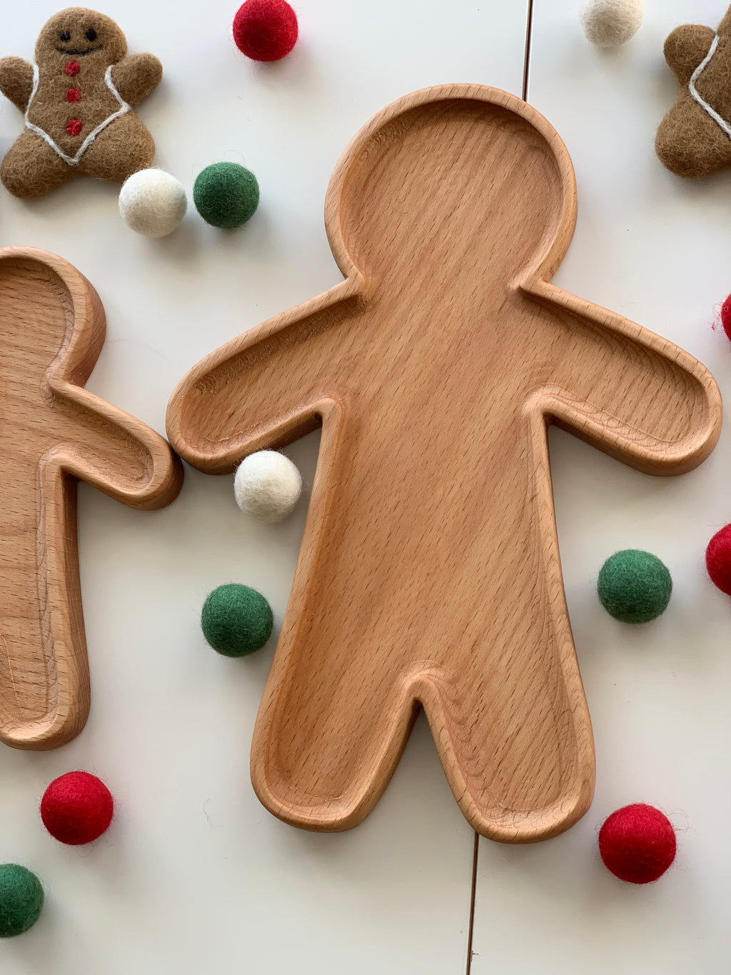 Large wooden person-shaped plate or sensory tray surrounded by colorful felt balls and gingerbread decorations