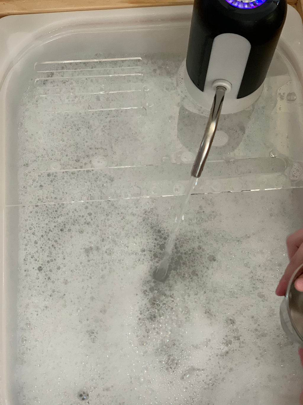 Play kitchen sink insert with water running from faucet into bubbly soap-filled basin on wooden surface