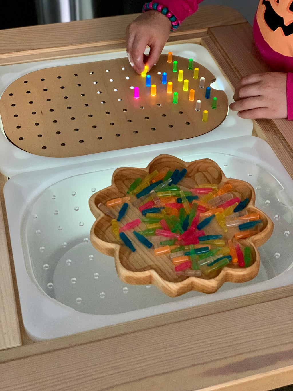 Child placing colorful plastic pegs into small hole geometric light board on wooden Flisat tabletop insert