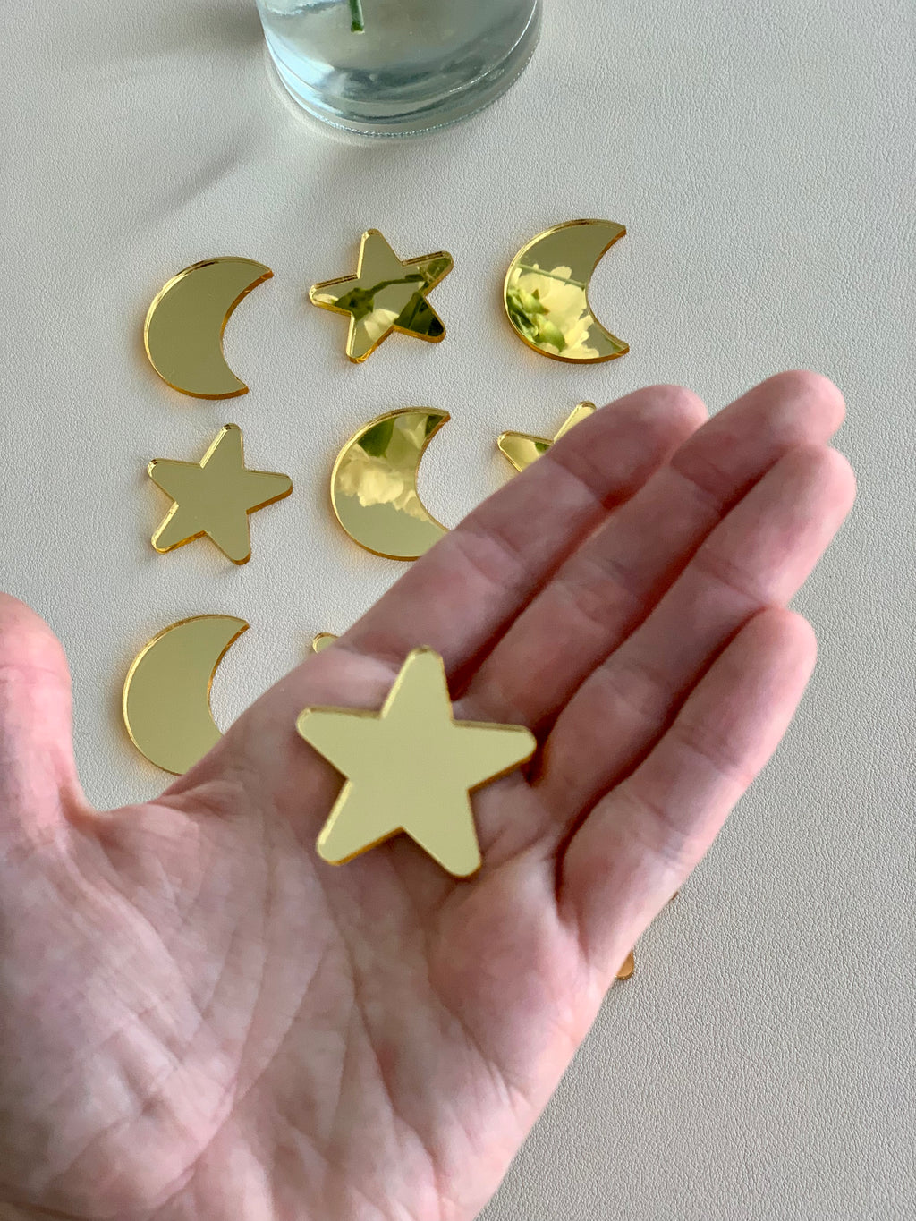 Hand holding shiny gold acrylic star shape with gold moon and star shapes scattered on white surface below