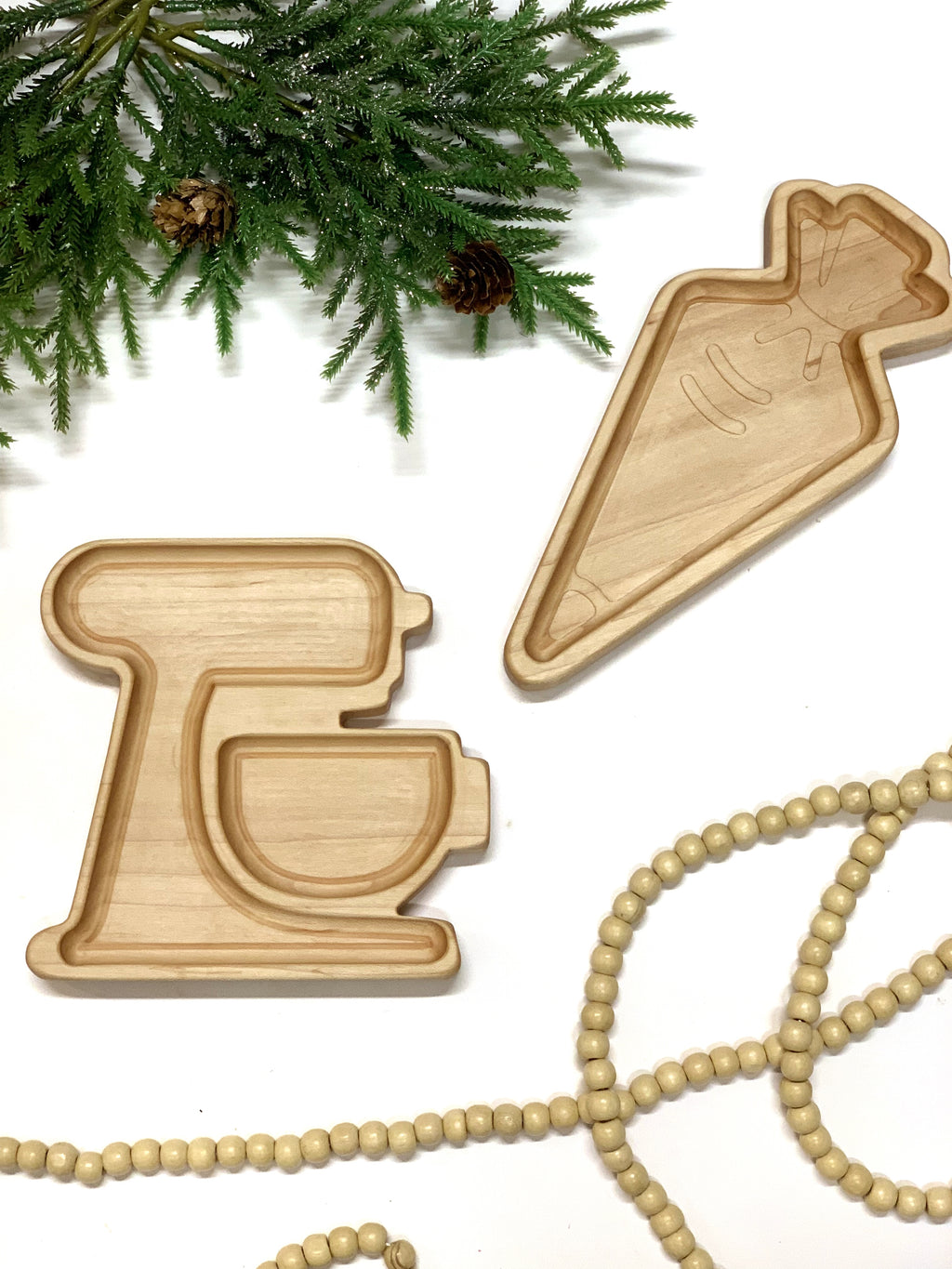 Natural wooden sensory trays shaped like a frosting bag and carrot plate displayed with pine greenery and wooden beads on white background