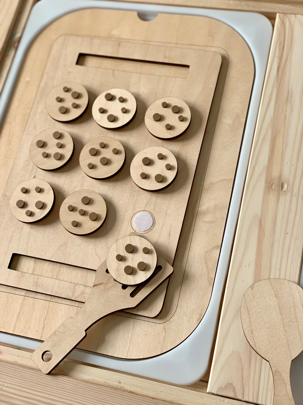 Wooden cookie sheet with nine circular cookies featuring wooden chips and a spatula on light wood surface