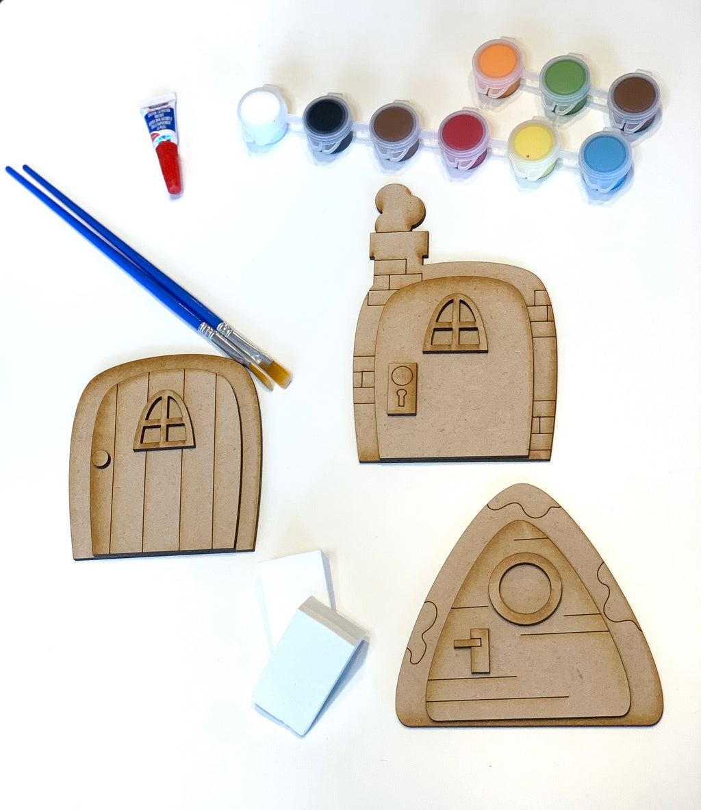 DIY kit with three unpainted wooden fairy doors, paint pots in various colors, brushes, and sponges on white background