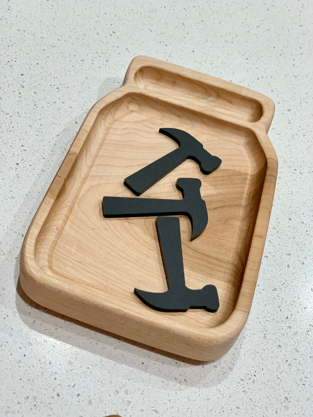 Wooden jar-shaped tray holding three black acrylic loose parts shaped like hammers on light countertop