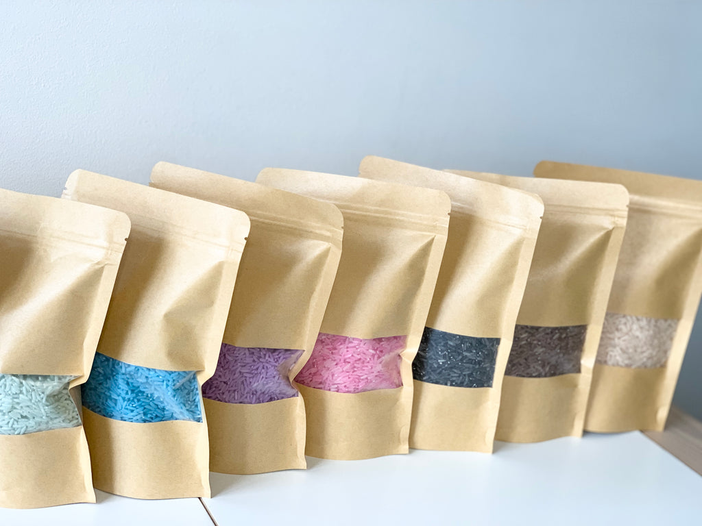 Kraft paper resealable bags filled with colourful sensory bin fillers in various shades on white surface