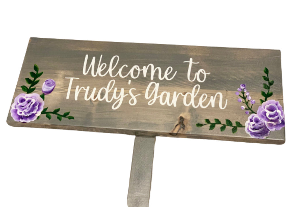 Large personalized wooden garden sign painted gray with white cursive letters and purple floral illustrations on wood background