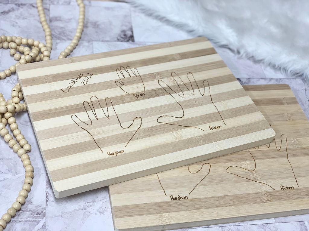 Personalized striped wooden cutting board with engraved handprints and names on light and dark wood grain background