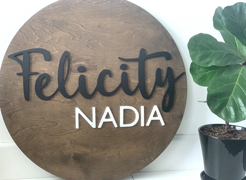 Large round wooden name sign stained brown with black cursive and white block letters on white background