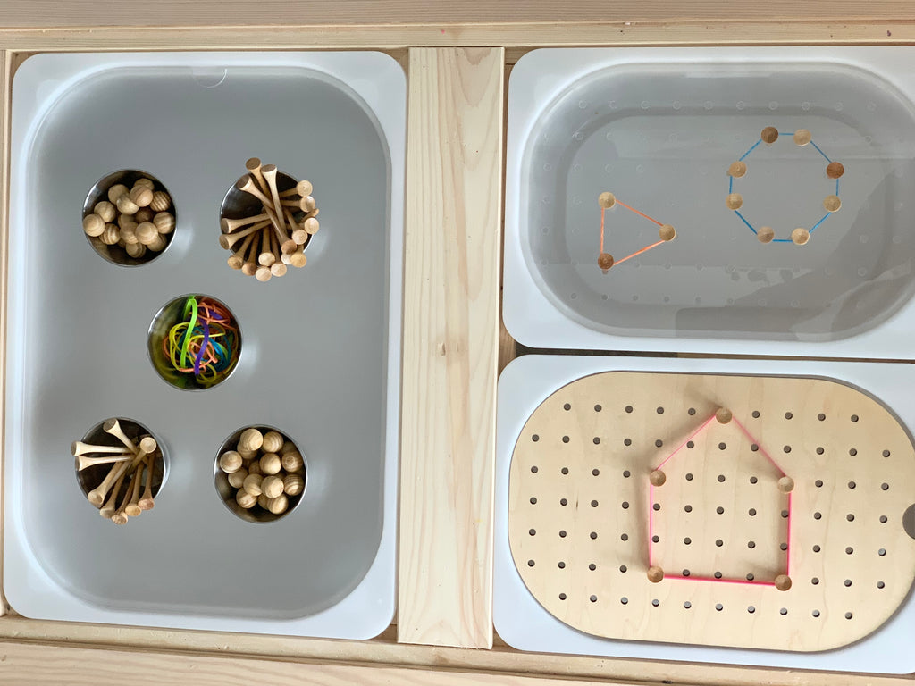 Light maple wood Flisat table insert with gray acrylic tray holding wooden pegs and colorful rubber bands on white surface