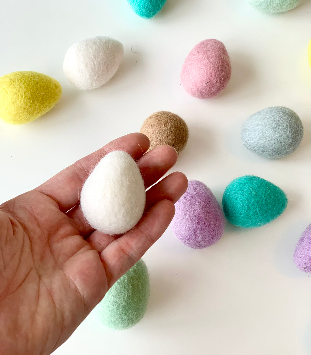 Hand holding one white felt Easter egg surrounded by colorful handmade wool felt eggs on white background