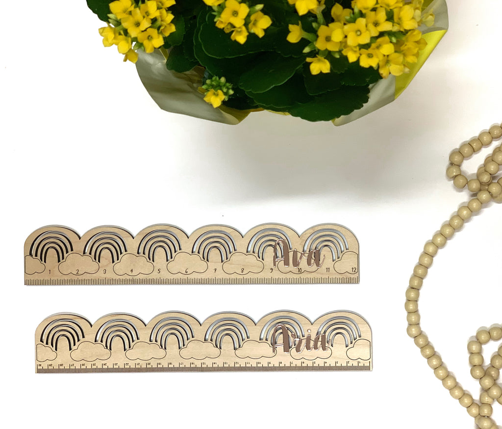 Natural wooden personalized rainbow rulers with engraved clouds and measurement marks on white background with yellow flowers