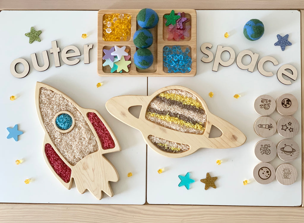 Wooden rocket ship and planet sensory trays with colorful fillers and wooden outer space letters on white table