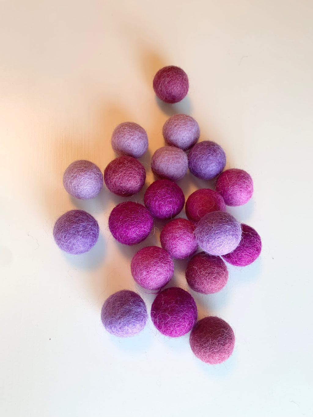 Assorted felt balls in various shades of purple and pink scattered on a white surface